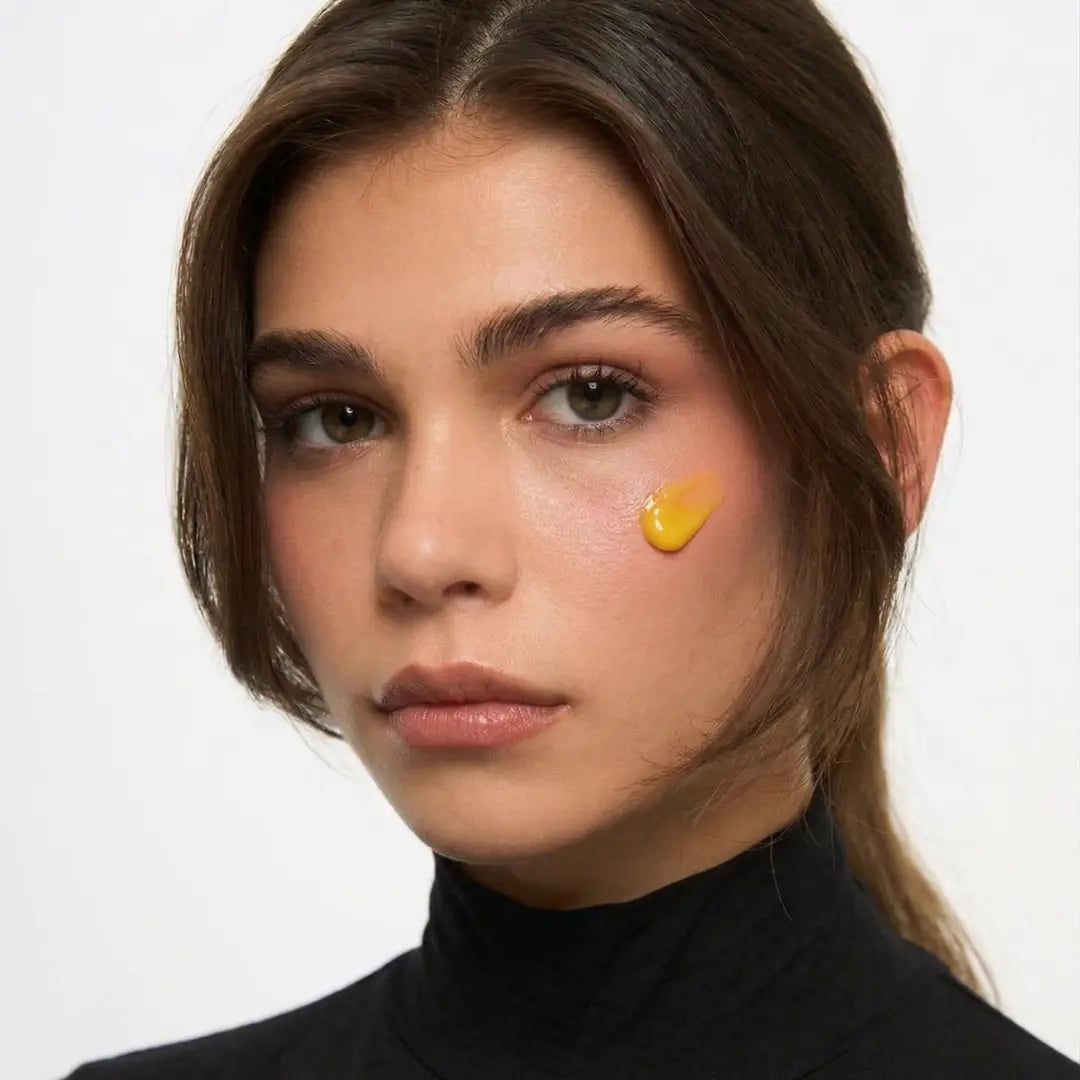 Woman with a yellow droplet of BY VALENTI Bakuchiol Night Repair Cream on her cheek against a white background