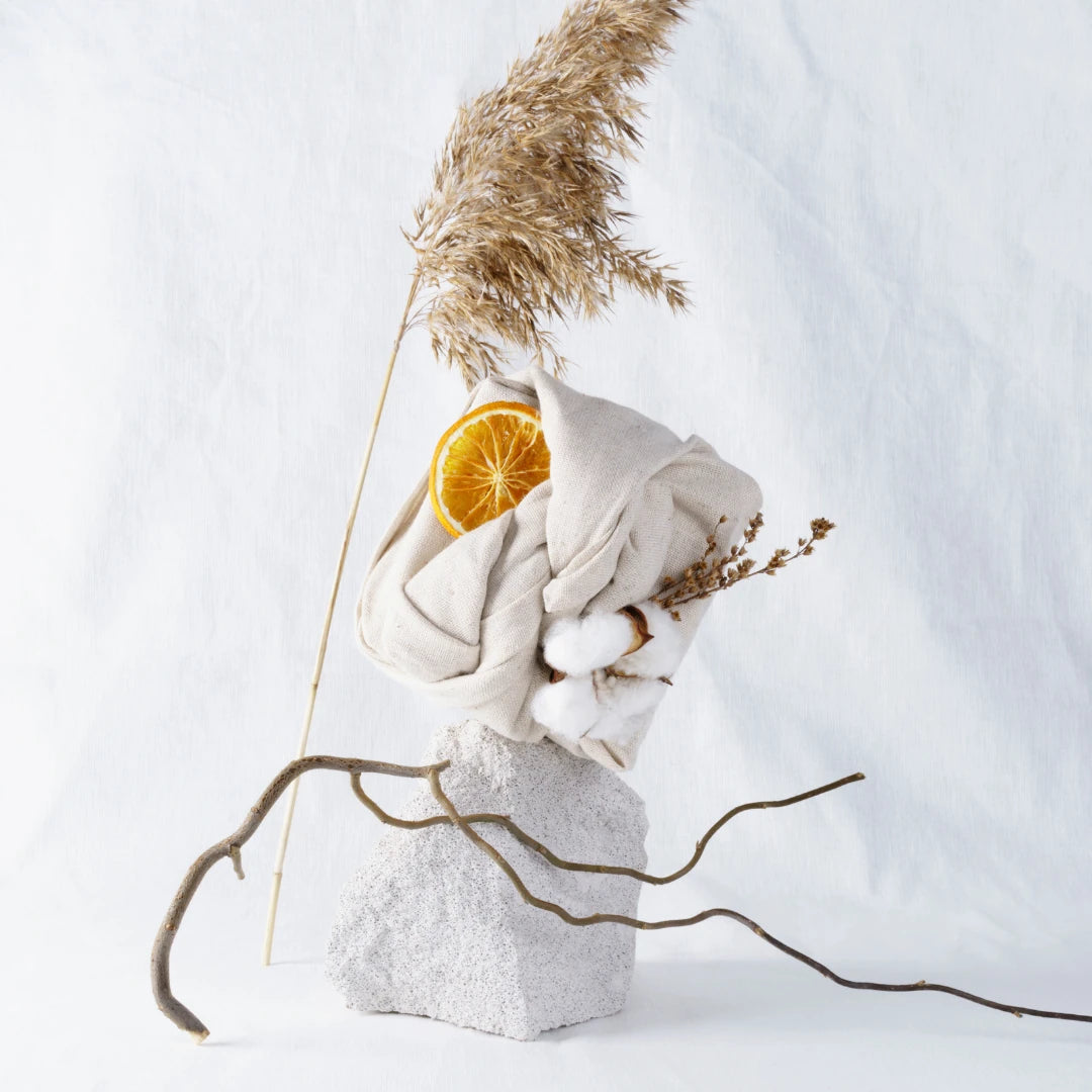 Decorative arrangement with dried plants, orange slice, and white fabric on a light background