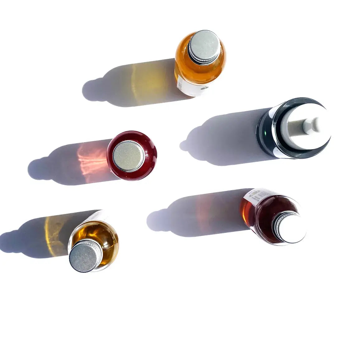 Four facial bottles of By Valenti serums with different colored liquids casting colorful shadows on a white background