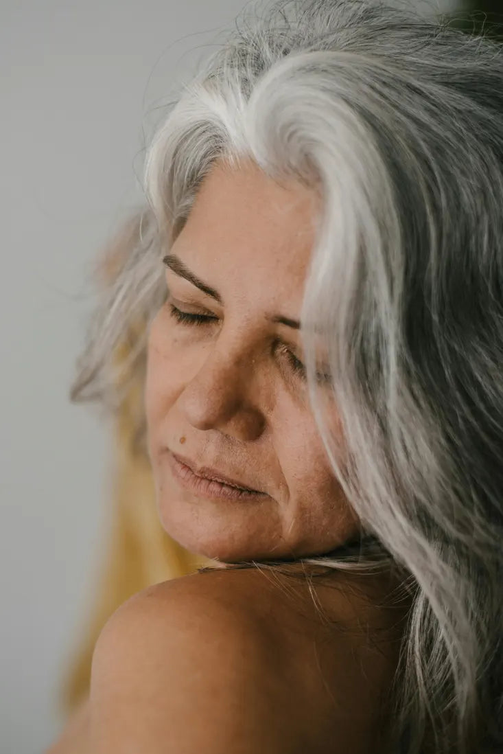 Woman with gray hair looking downwards against a neutral background