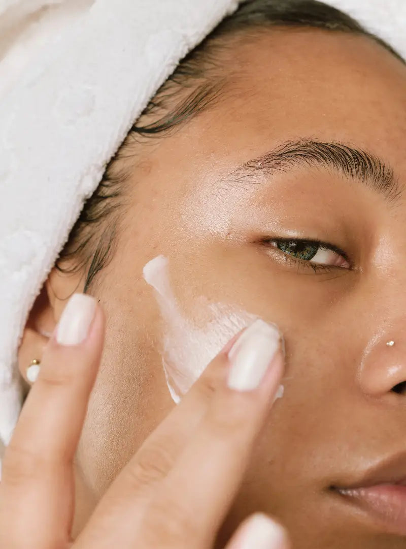 Woman applying cream to her face with a towel on her head